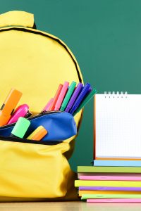 Backpack with school supplies and blank notepad on chalkboard background